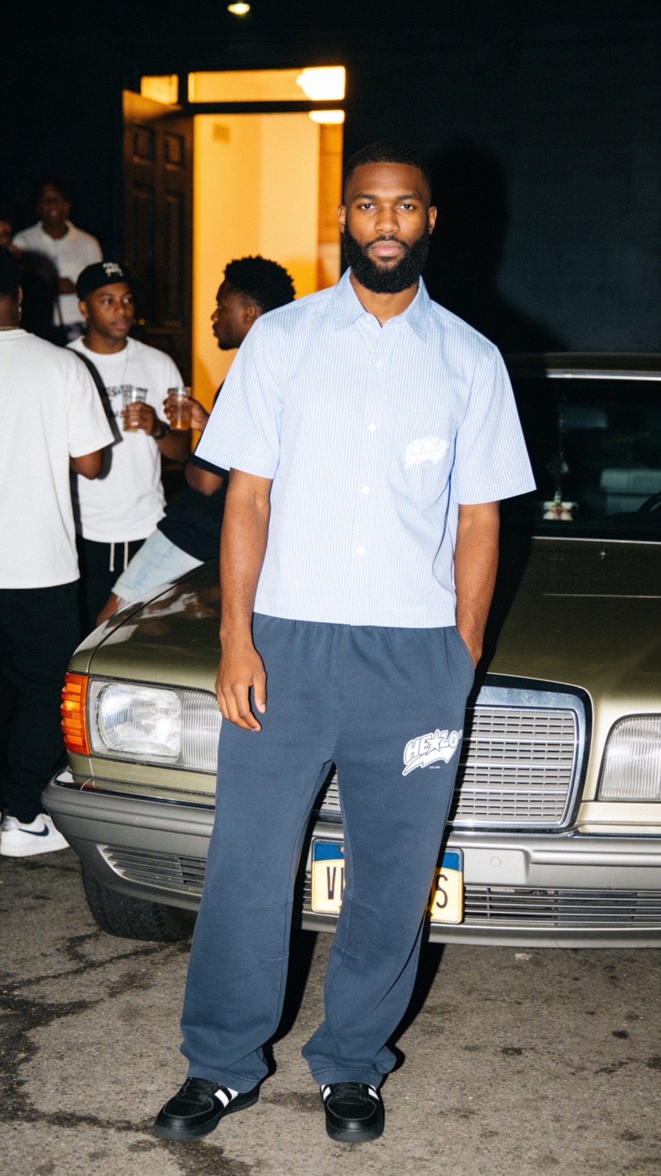 Footprint Apparel — bearded man wearing the light-blue striped button-up and navy HE★LO sweatpants in front of a vintage Mercedes at night