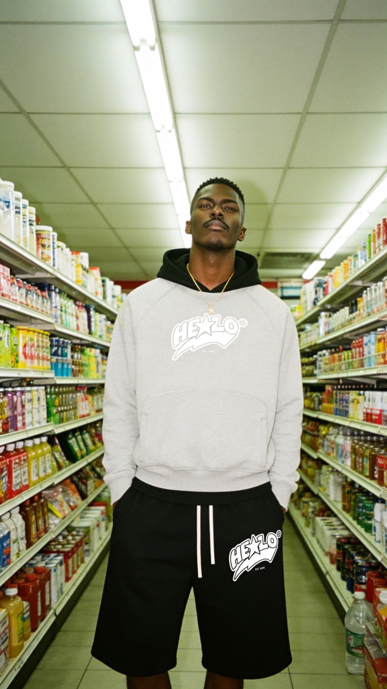 Footprint Apparel men's streetwear — man in a gray HE★LO hoodie and black shorts in a grocery aisle