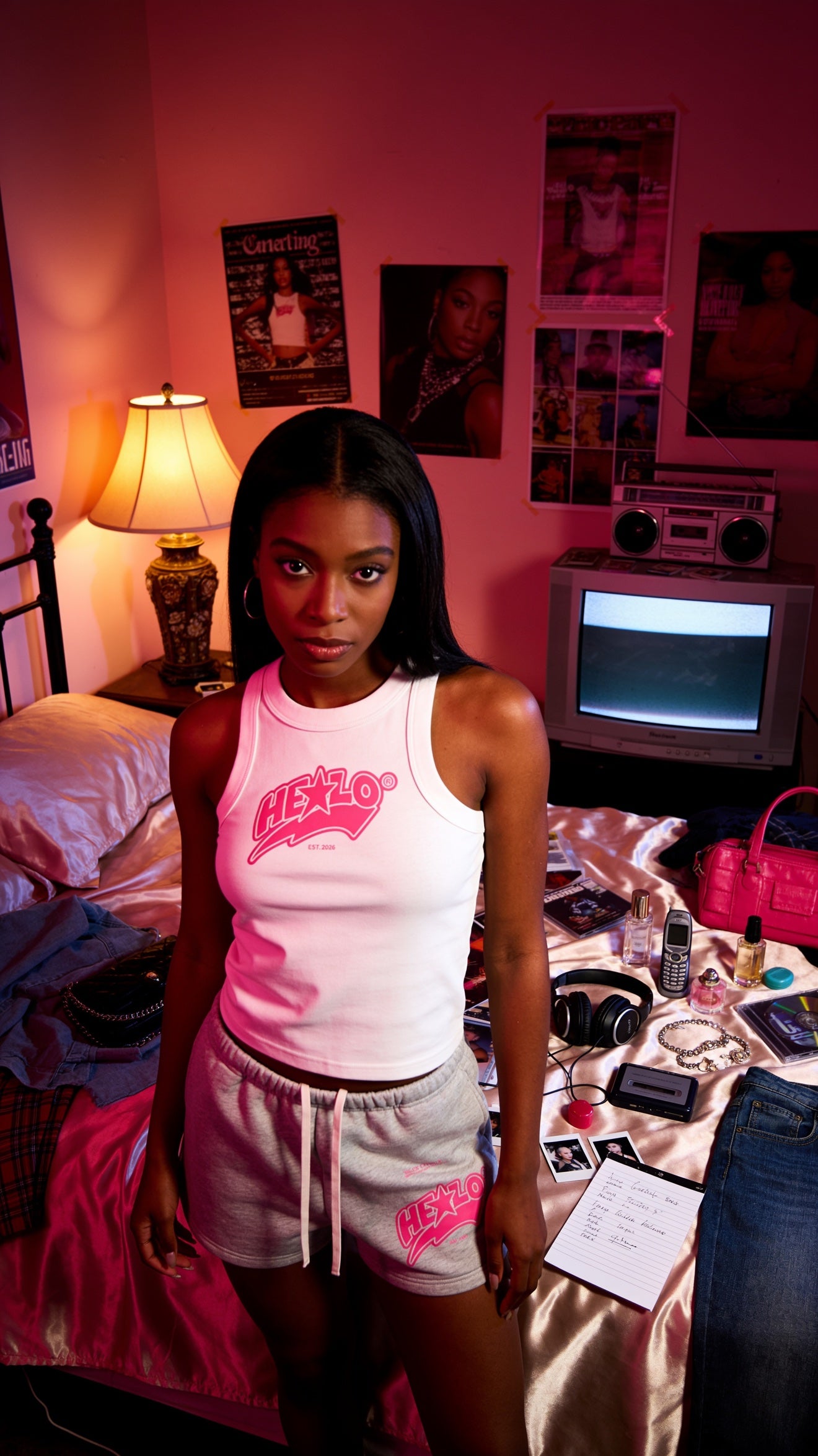 Footprint Apparel — woman wearing the white HE★LO tank top and gray HE★LO sweat shorts in a pink-lit bedroom