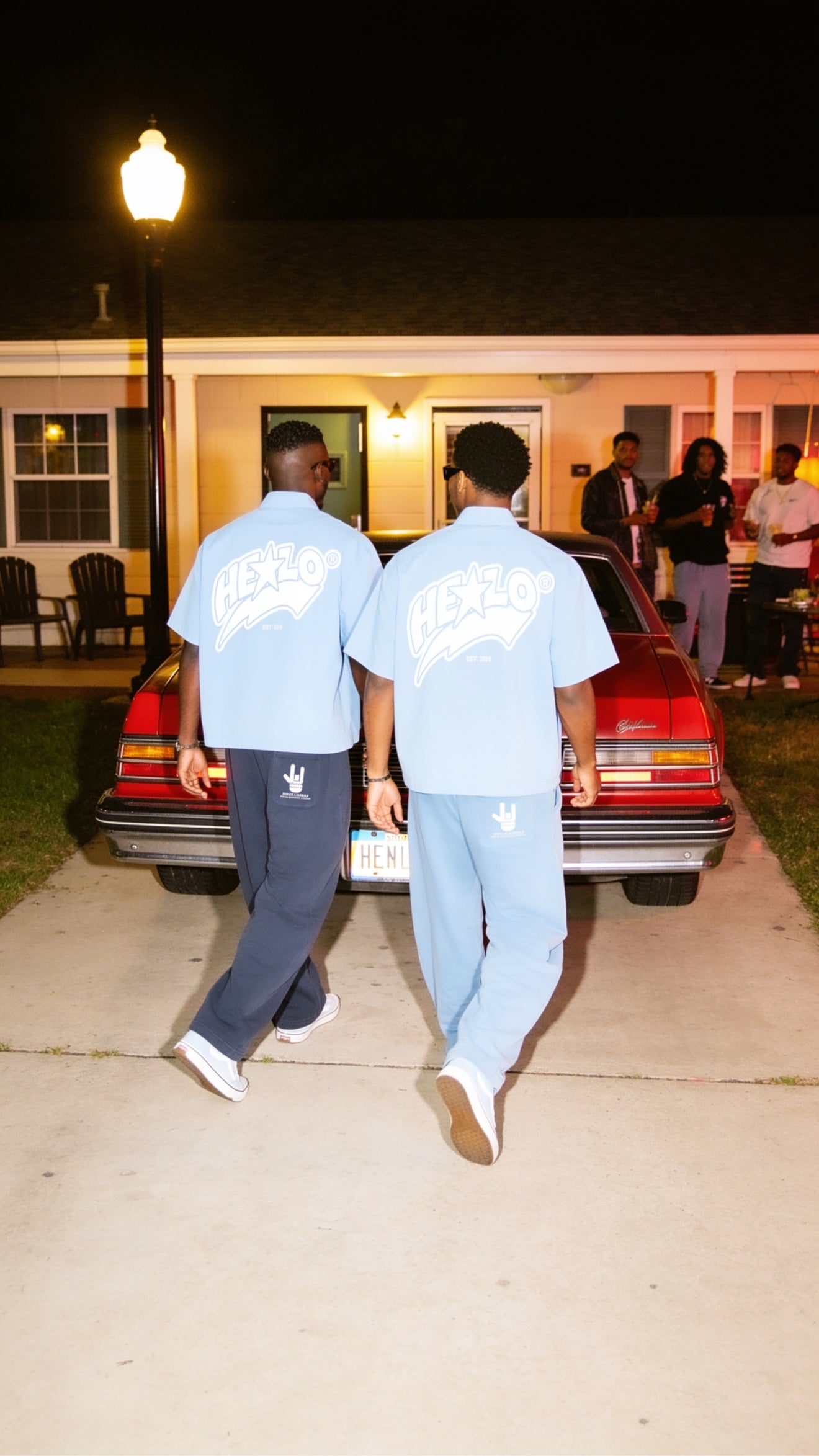 Two models in light blue HELLO sets by a red car at night
