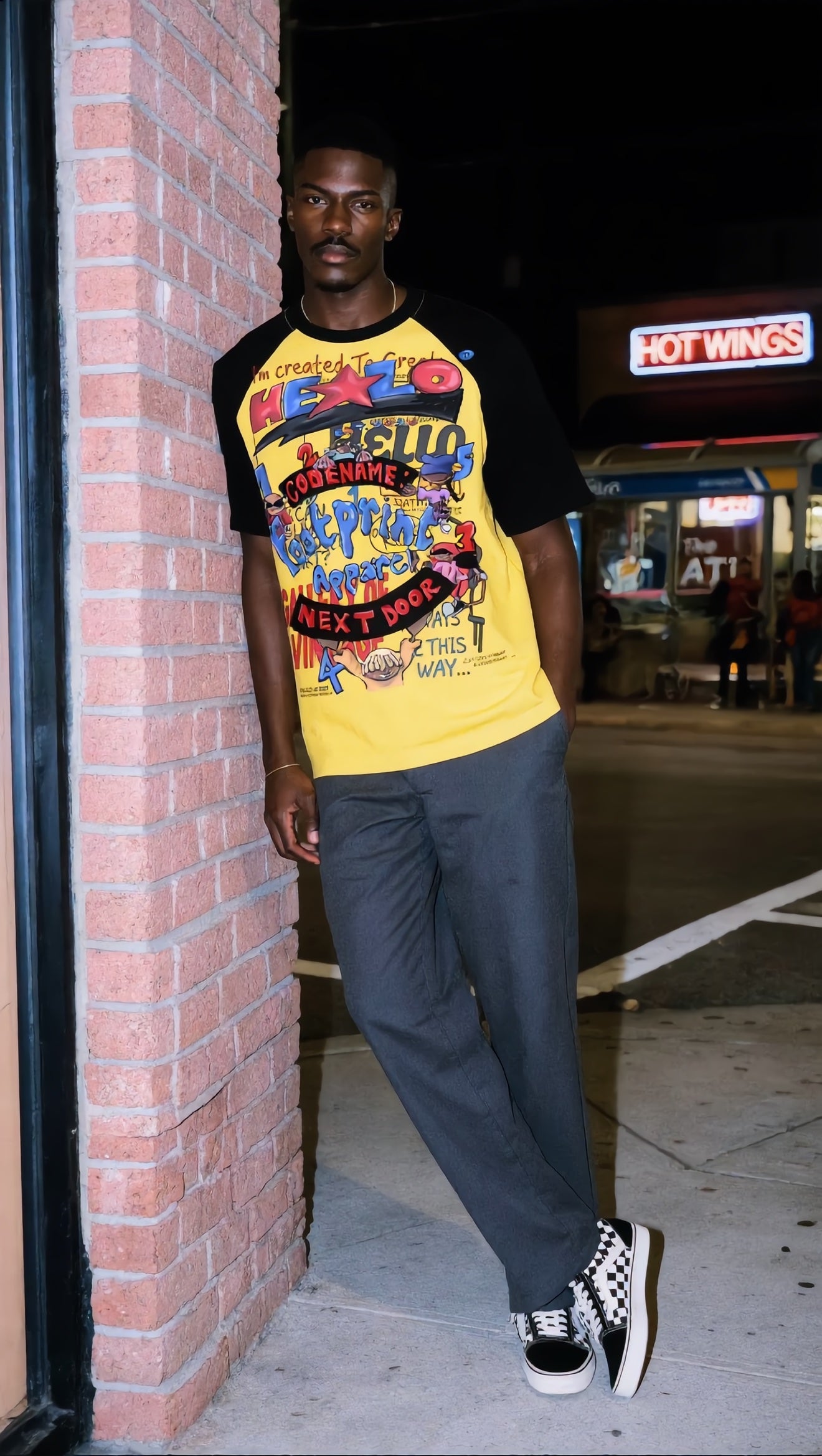 Footprint Apparel — Model A full body against a brick wall wearing the yellow raglan tee