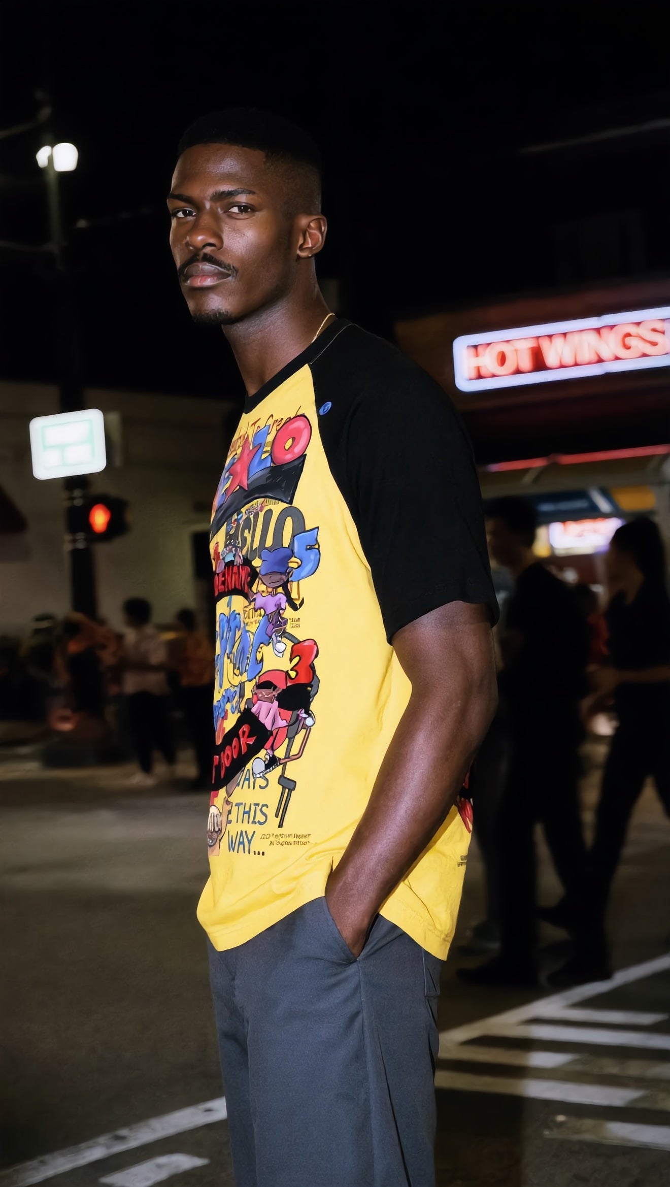 Footprint Apparel — Model A in profile wearing the yellow and black raglan tee at night under a HOT WINGS sign